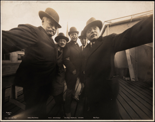 Five photographers posing together for a photograph on the roof of Marceau's Studio, while Joseph Byron holds one side of the camera with his right hand and Ben Falk holds the other side with his left hand.